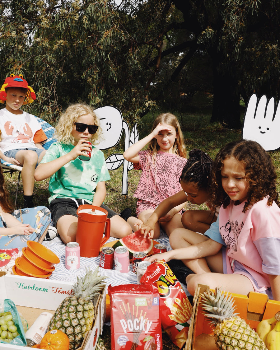 Kids having a summer picnic in the park wearing Minti kids clothes, printed tees, shorts and matching sets
