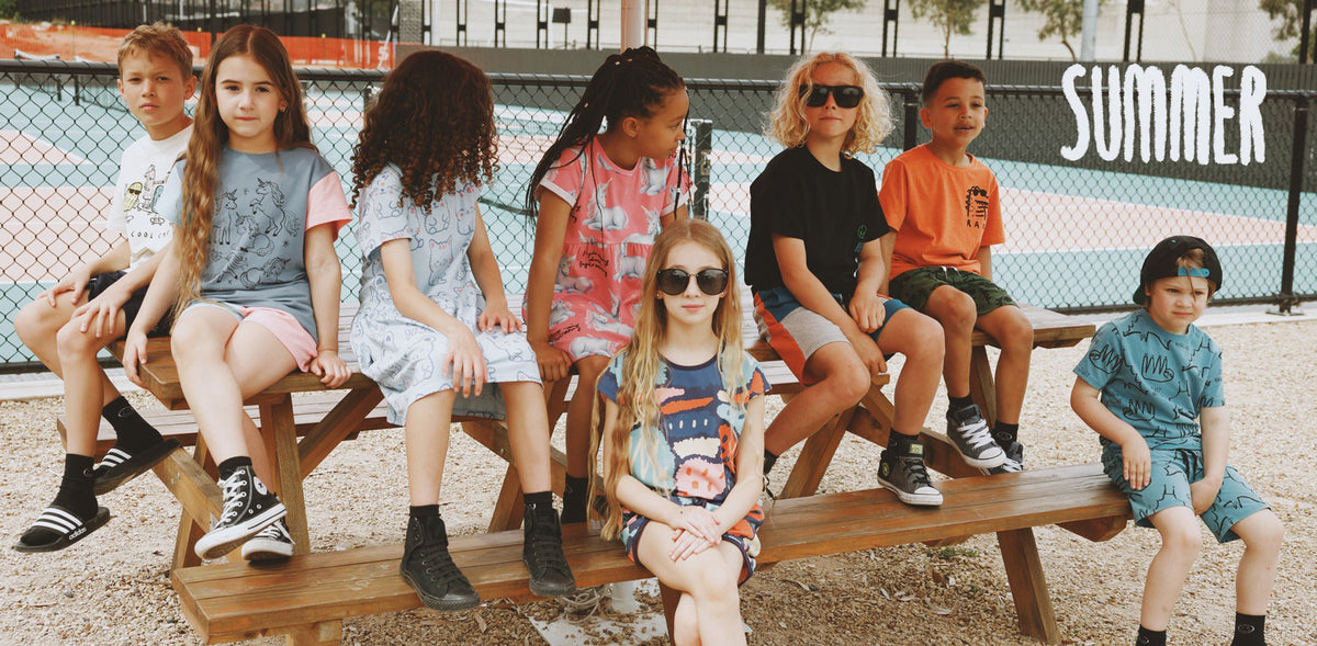 Kids sitting on a picnic table in Minti summer clothes